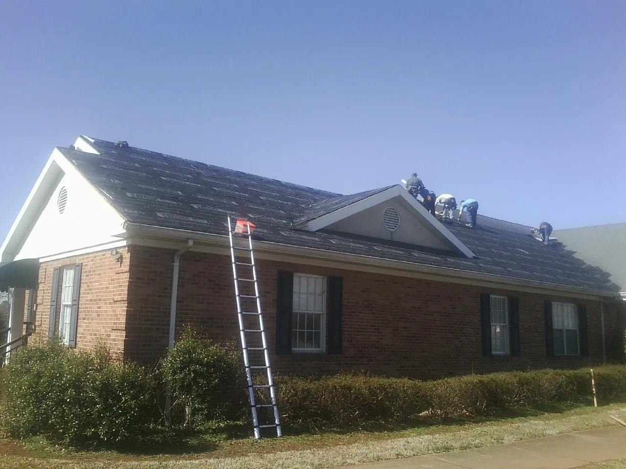 Crew tearing shingles off a brick ranch roof with a ladder set — Emergency Roof Repair work by our crew in Mitchell