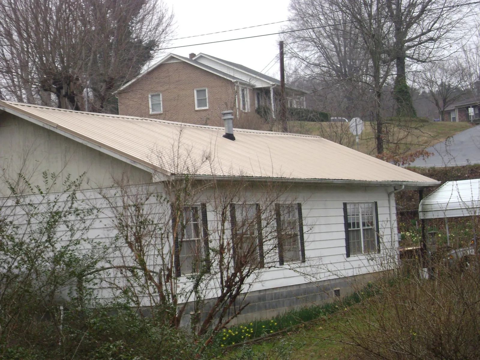 Tan metal roof on a white sided house set into a hillside — Commercial Roofing by Roofing Brothers in Mitchell